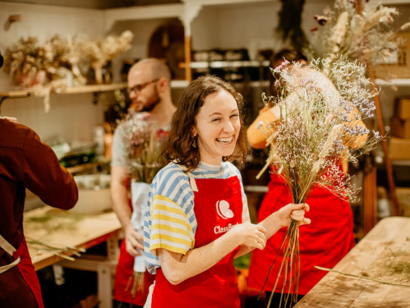 A woman smiles whilst holding a dried flower bouquet created at a flower arranging class